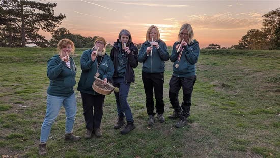 Five forest-school leaders playing whittled whistles together at sunset
