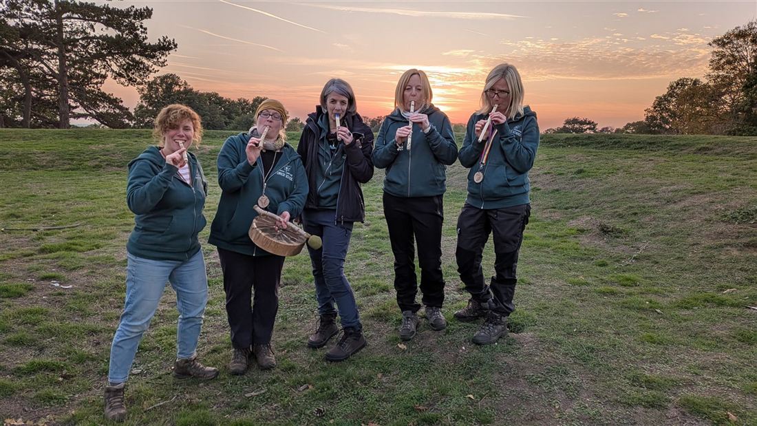 Five forest-school leaders playing whittled whistles together at sunset