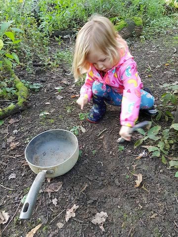 A child crouched on the forest floor, digging beside an old saucepan