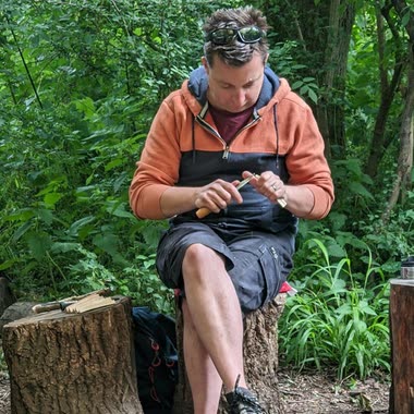 A leader whittling with a knife on a log seat in the woods